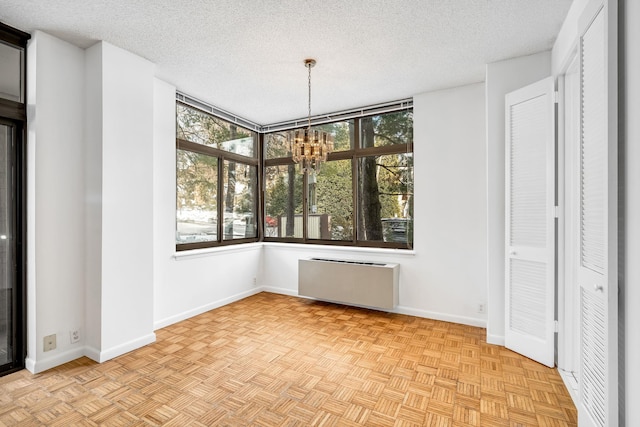 unfurnished dining area with light parquet floors, a textured ceiling, radiator, and an inviting chandelier