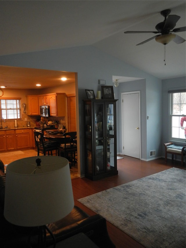 living area featuring lofted ceiling, a healthy amount of sunlight, visible vents, and wood finished floors