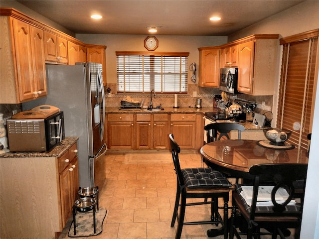 kitchen with tasteful backsplash, recessed lighting, stainless steel microwave, a sink, and dark stone counters