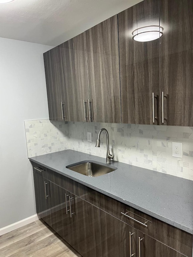 kitchen with backsplash, sink, light wood-type flooring, light stone counters, and dark brown cabinetry