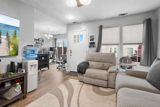 living room featuring ceiling fan with notable chandelier, a textured ceiling, and light hardwood / wood-style flooring