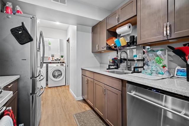 kitchen featuring light stone countertops, sink, stainless steel appliances, light hardwood / wood-style flooring, and washer / dryer