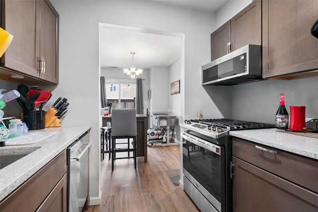 kitchen with an inviting chandelier, light hardwood / wood-style flooring, light stone countertops, appliances with stainless steel finishes, and decorative light fixtures