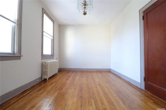 empty room with light wood-type flooring, radiator, and a notable chandelier