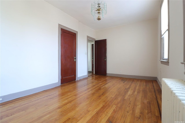 spare room featuring radiator heating unit, a notable chandelier, and light hardwood / wood-style flooring