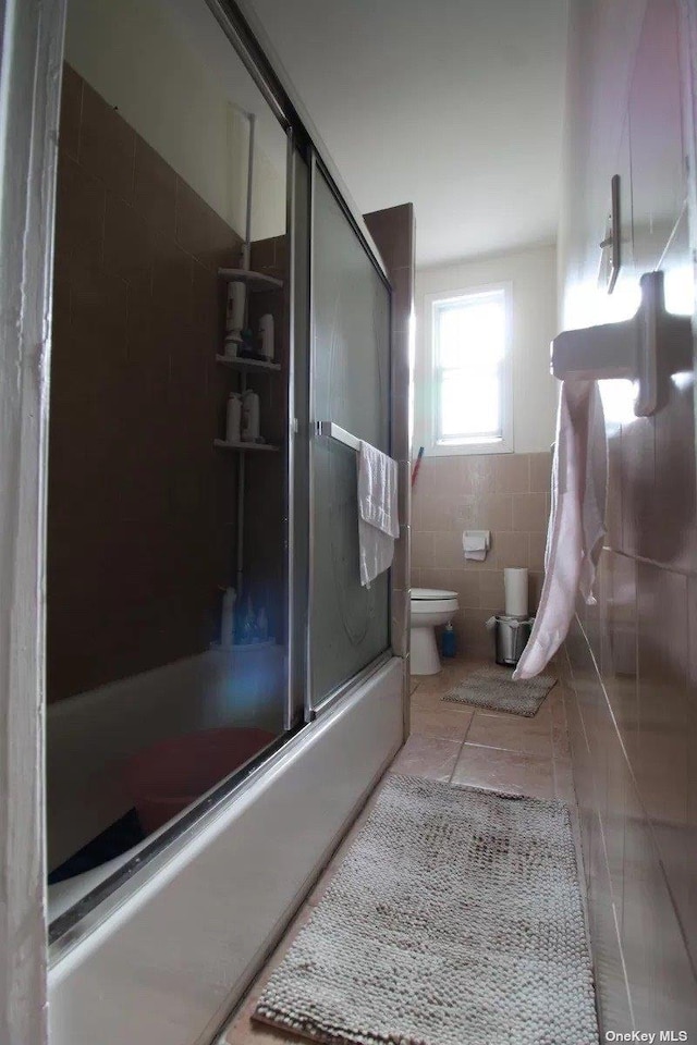 bathroom with tile patterned flooring, toilet, combined bath / shower with glass door, and tile walls