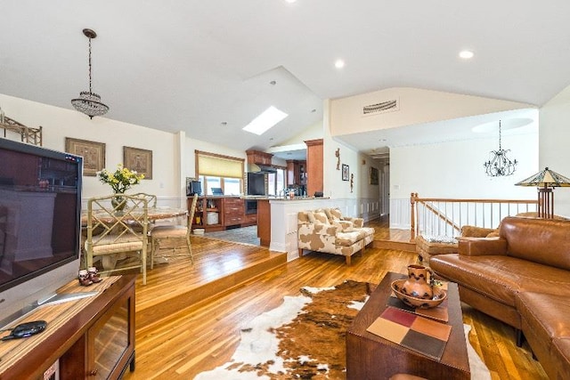 living room featuring vaulted ceiling with skylight, a notable chandelier, and light hardwood / wood-style flooring