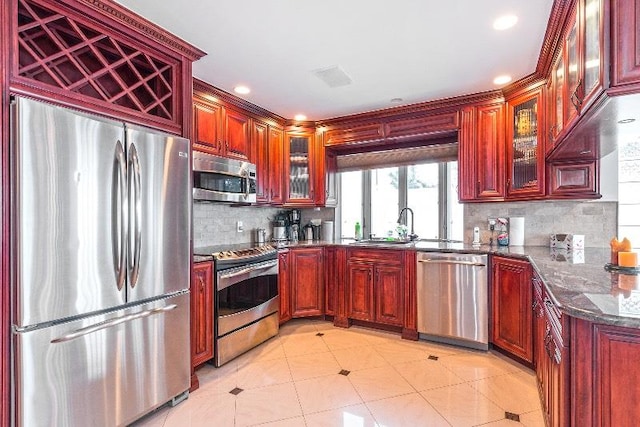 kitchen featuring sink, tasteful backsplash, dark stone counters, light tile patterned flooring, and appliances with stainless steel finishes