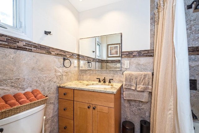 bathroom with vanity, toilet, and tile walls