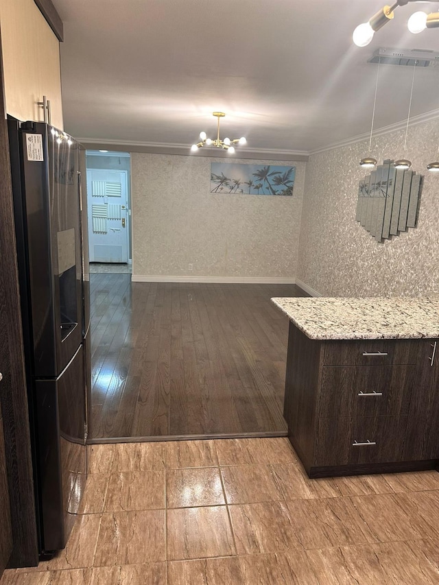 kitchen with light stone counters, crown molding, stainless steel fridge, dark brown cabinets, and light wood-type flooring