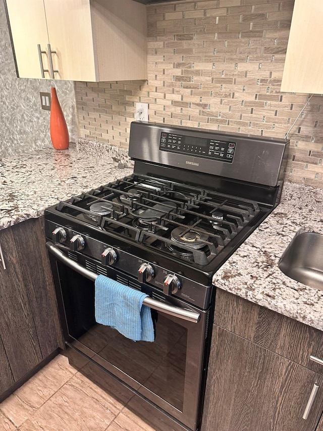 kitchen with backsplash, gas range, cream cabinetry, light stone counters, and dark brown cabinetry