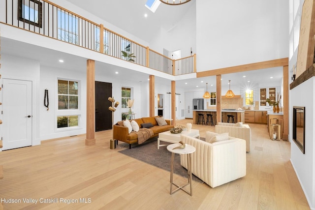 living room with a skylight, a towering ceiling, and light hardwood / wood-style flooring