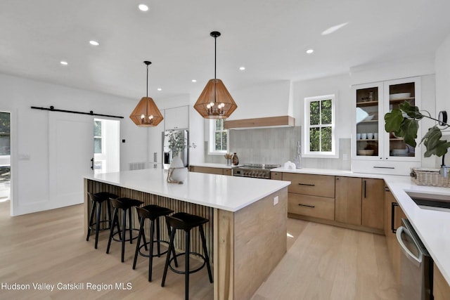 kitchen featuring a barn door, light hardwood / wood-style floors, decorative light fixtures, appliances with stainless steel finishes, and custom exhaust hood