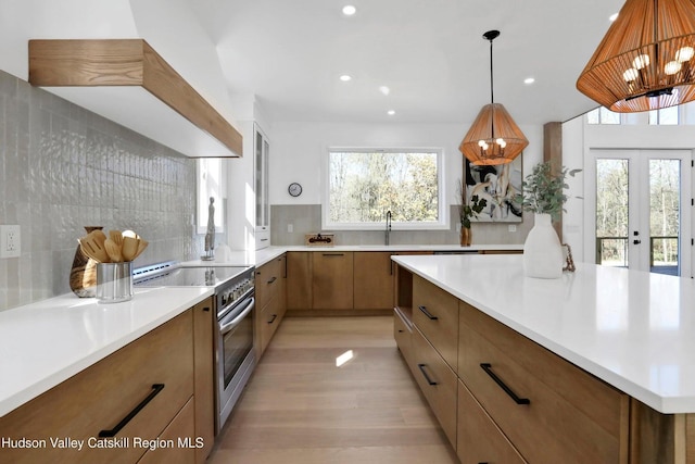 kitchen featuring decorative backsplash, premium range hood, pendant lighting, light hardwood / wood-style flooring, and stainless steel electric range oven