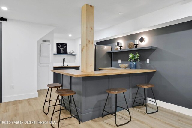 kitchen with kitchen peninsula, stainless steel fridge, light wood-type flooring, and a breakfast bar area