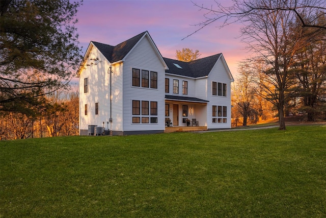 back house at dusk featuring a lawn, cooling unit, and covered porch