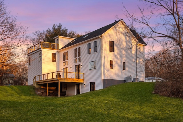 back house at dusk featuring a lawn, a balcony, and central air condition unit