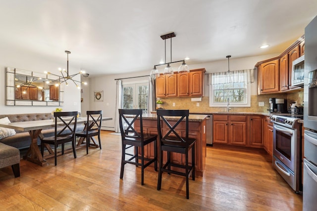 kitchen with a kitchen island, a breakfast bar, pendant lighting, stainless steel appliances, and light hardwood / wood-style flooring