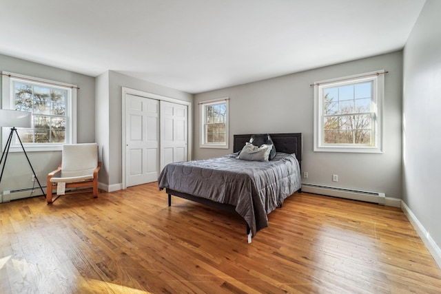 bedroom featuring a baseboard radiator, a closet, multiple windows, and light wood-type flooring