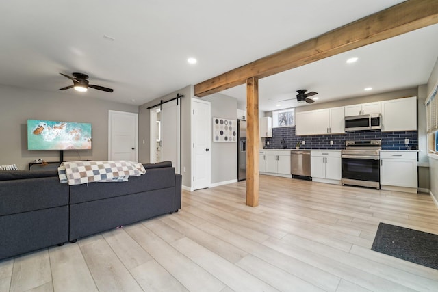 living room with sink, a barn door, ceiling fan, and light wood-type flooring