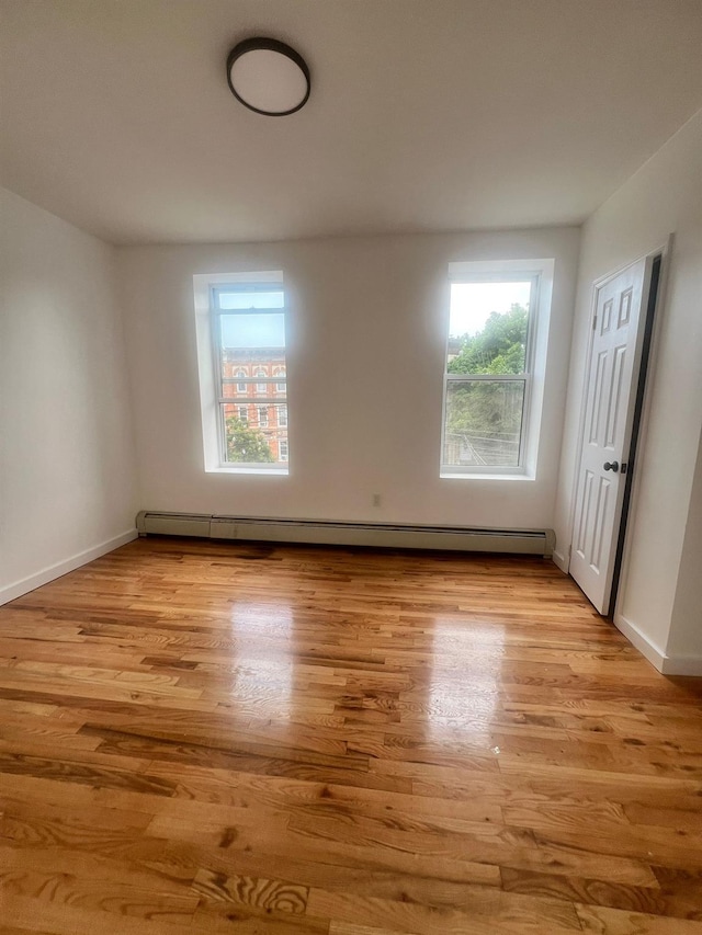 empty room with baseboard heating and light hardwood / wood-style flooring