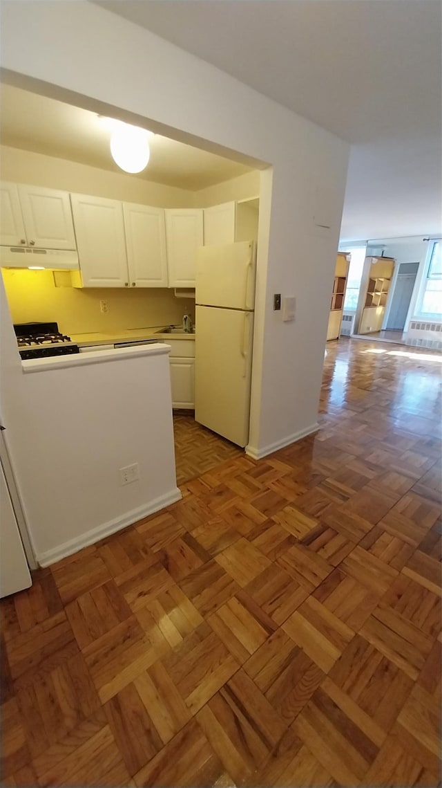 kitchen with light parquet floors, white refrigerator, and white cabinetry