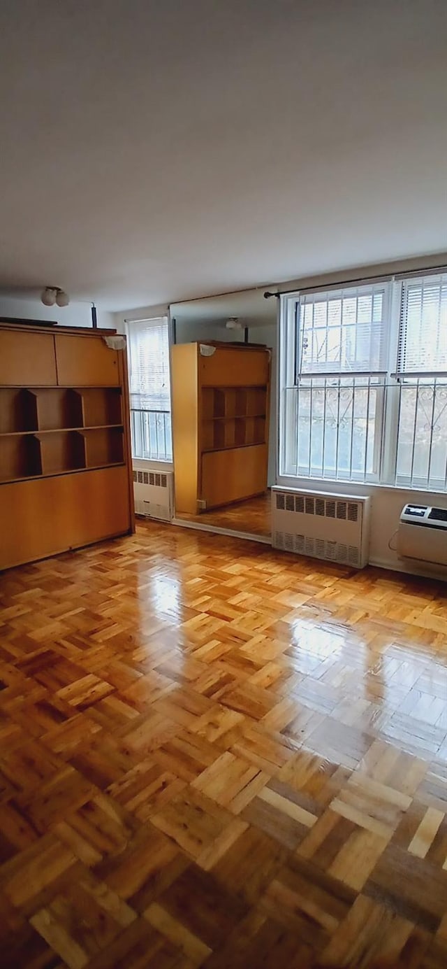 unfurnished living room featuring radiator and an AC wall unit