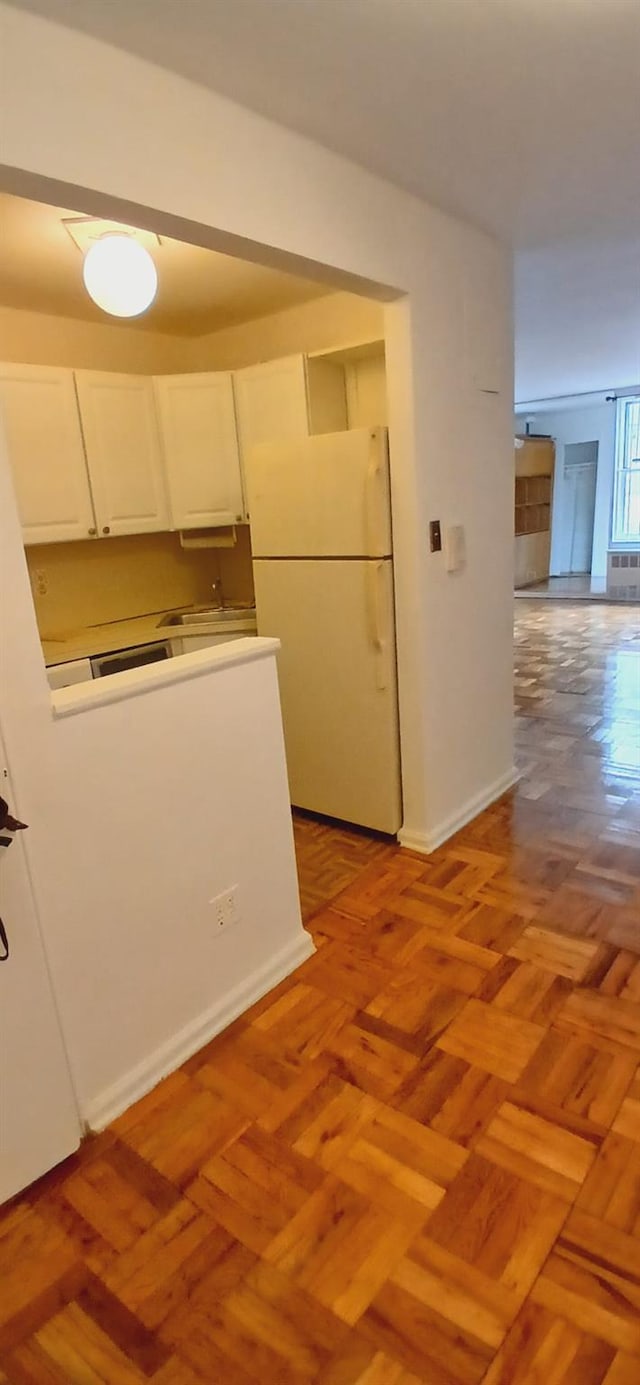 kitchen featuring baseboards, freestanding refrigerator, and white cabinetry