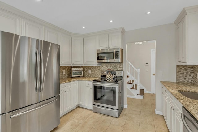 kitchen featuring decorative backsplash, light stone counters, white cabinets, and stainless steel appliances