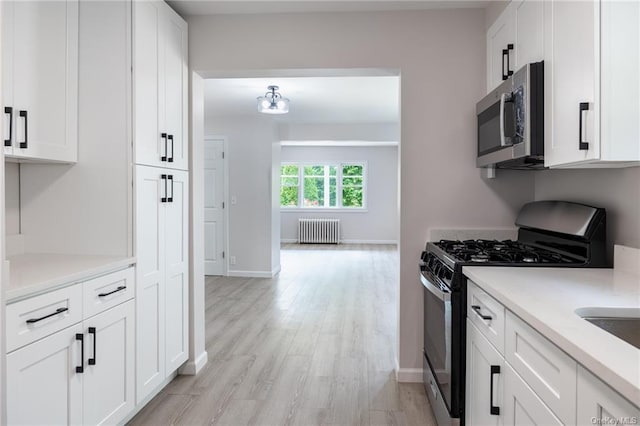 kitchen featuring appliances with stainless steel finishes, light hardwood / wood-style floors, white cabinetry, and radiator