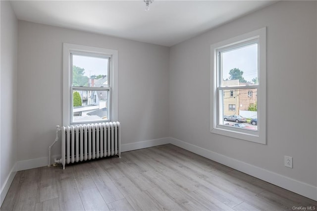 spare room with radiator heating unit, plenty of natural light, and light wood-type flooring