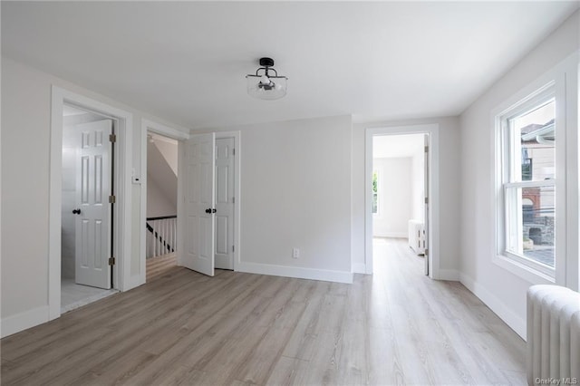 unfurnished room featuring a wealth of natural light, radiator heating unit, and light hardwood / wood-style floors