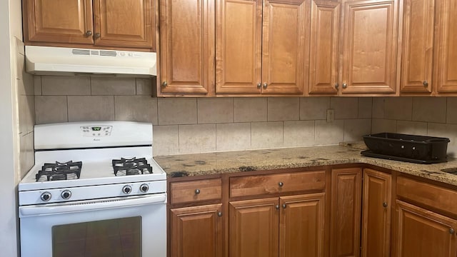 kitchen featuring tasteful backsplash, light stone counters, and white range with gas stovetop