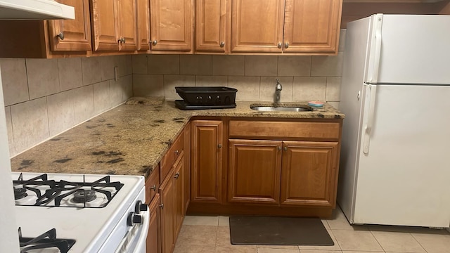 kitchen featuring sink, light stone counters, light tile patterned floors, white appliances, and backsplash