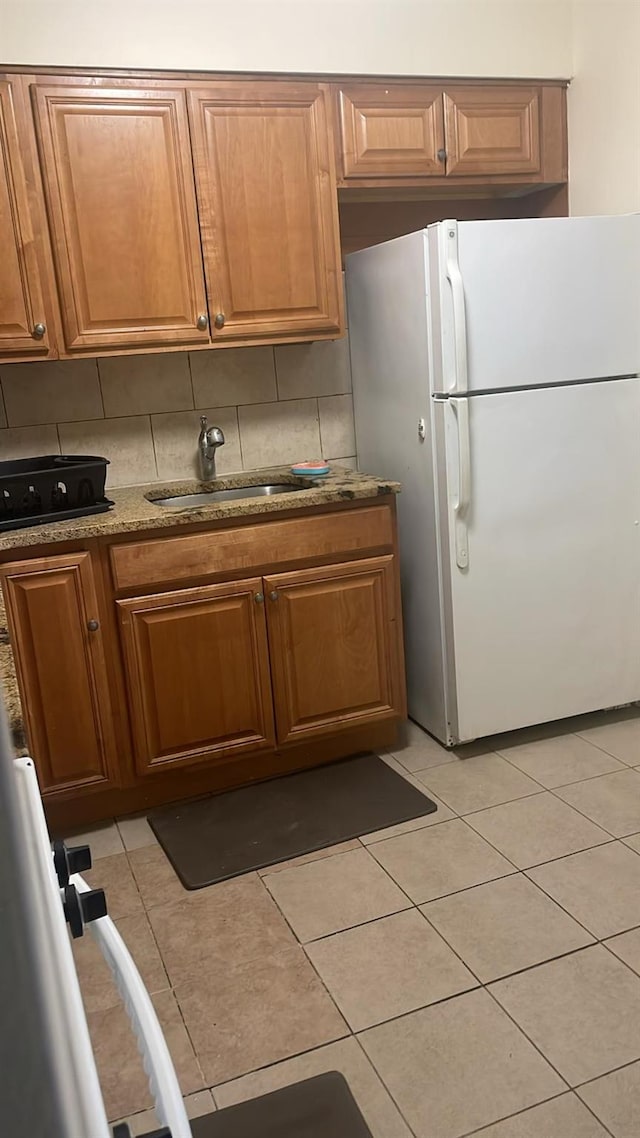 kitchen featuring white refrigerator, light tile patterned flooring, sink, and backsplash