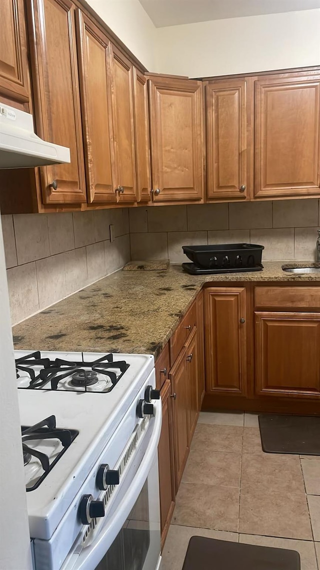 kitchen with sink, white range with gas stovetop, backsplash, light stone countertops, and light tile patterned flooring