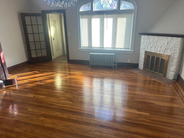 unfurnished living room featuring radiator, a fireplace, dark hardwood / wood-style floors, and a notable chandelier