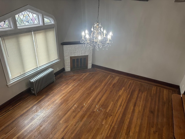 unfurnished living room featuring a notable chandelier, wood-type flooring, a fireplace, and radiator