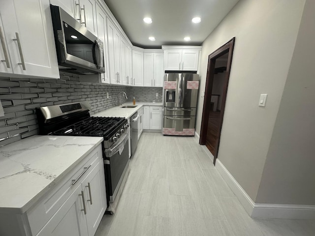 kitchen featuring light stone countertops, appliances with stainless steel finishes, tasteful backsplash, sink, and white cabinetry