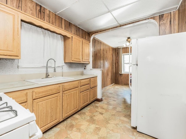 kitchen with wood walls, white appliances, sink, ceiling fan, and light brown cabinetry