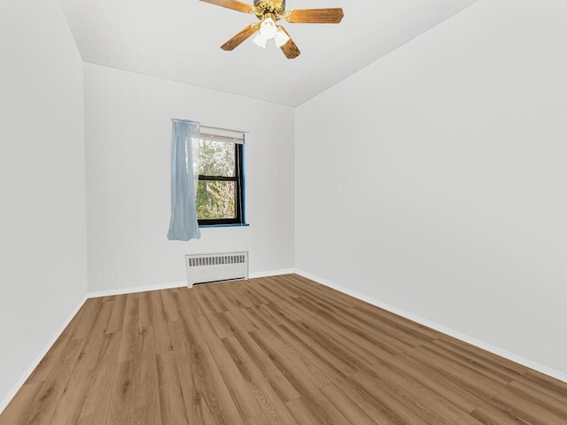 empty room featuring ceiling fan, light hardwood / wood-style floors, lofted ceiling, and radiator