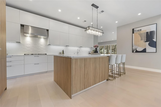 kitchen featuring a large island with sink, white cabinets, and wall chimney exhaust hood