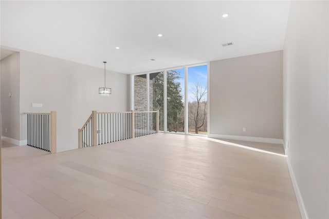 unfurnished room featuring expansive windows, light wood-type flooring, and an inviting chandelier