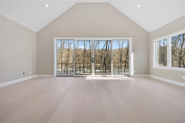 unfurnished living room featuring a wealth of natural light, light hardwood / wood-style flooring, and a towering ceiling