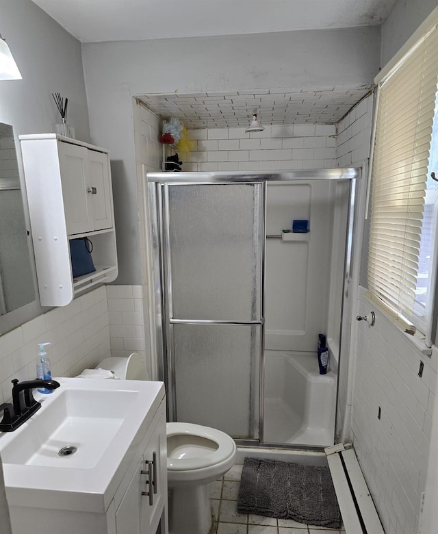 bathroom featuring vanity, a shower with door, tile walls, tile patterned flooring, and toilet