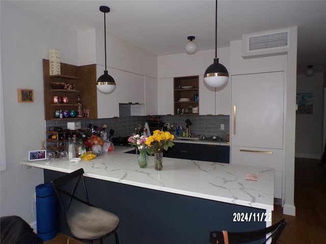 kitchen featuring kitchen peninsula, tasteful backsplash, white cabinetry, hanging light fixtures, and a breakfast bar area