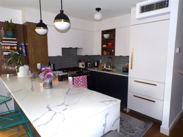 kitchen with stainless steel gas range oven, white cabinets, sink, decorative backsplash, and decorative light fixtures