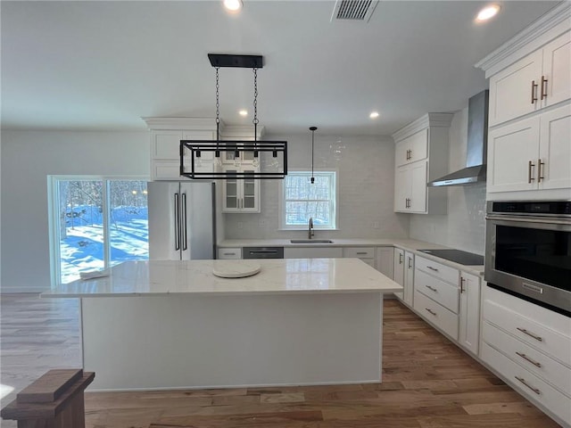 kitchen with wall chimney exhaust hood, stainless steel appliances, sink, pendant lighting, and a center island