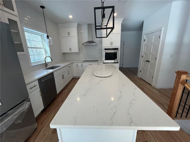 kitchen with white cabinetry, sink, wall chimney exhaust hood, a kitchen island, and black appliances