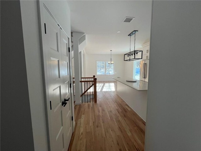 corridor with light wood-type flooring and a chandelier